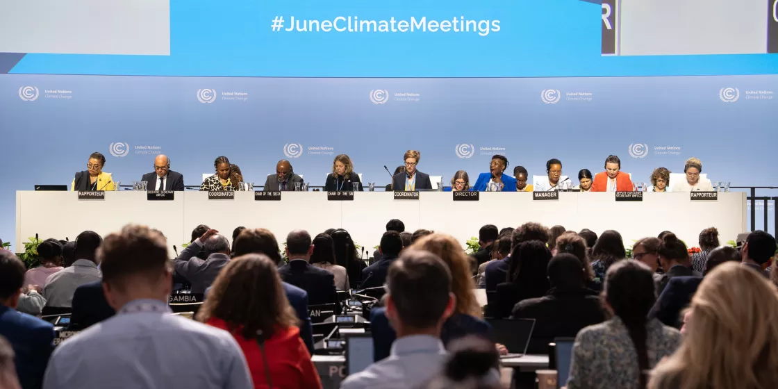 Bei den SB Klima-Zwischenverhandlungen sitzen Diskutierende auf einem Podium vor einer Menge an Zuhörer:innen. Im Hintergrund steht #JuneClimateMeetings