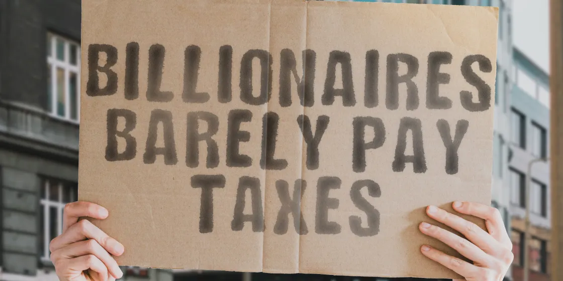 Zwei Hände halten ein Protestschild mit der Aufschrift "Billionaires barely pay taxes"