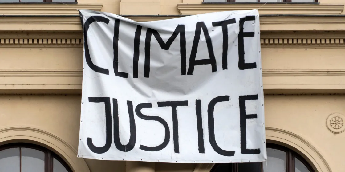 Eine Protestfahne hängt vor einem Gebäude mit der Aufschrift "Climate Justice" (Klimagerechtigkeit)