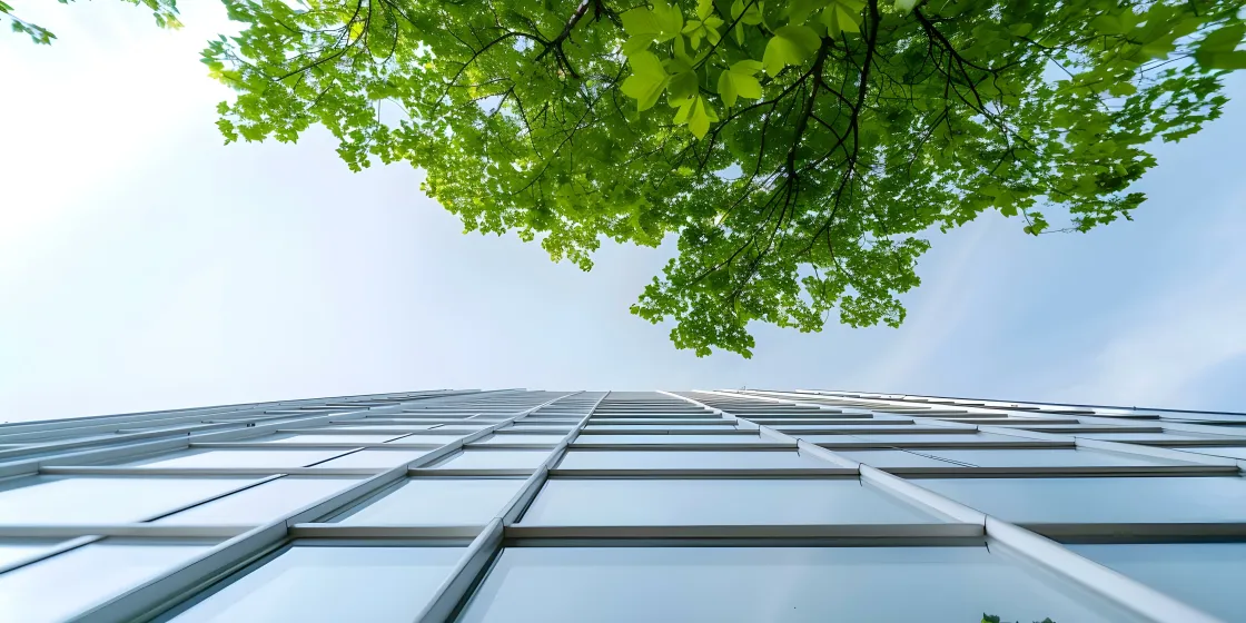 Sicht von unten auf einen in die Höhe ragenden Wolkenkratzer und einen grünen Baum