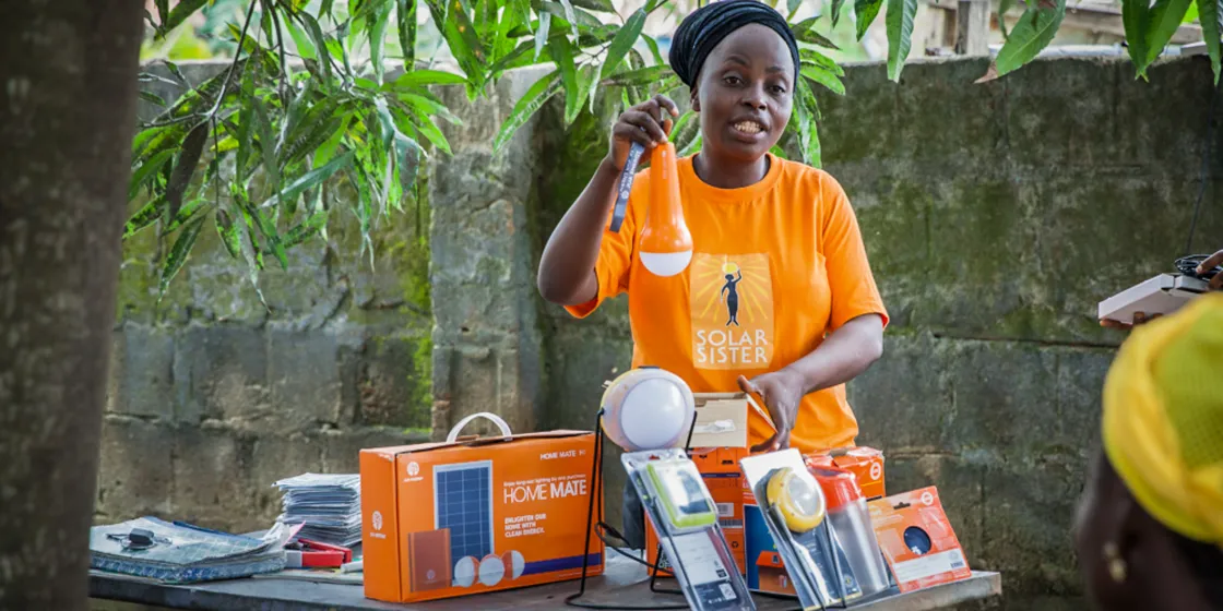 Eine Frau in einem Shirt der Solar Sisters hält eine Glühbirne hoch