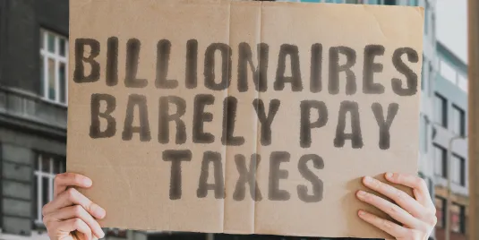 Zwei Hände halten ein Protestschild mit der Aufschrift "Billionaires barely pay taxes"