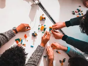 Menschen sitzen an einem Tisch und bauen mit Lego etwas zusammen