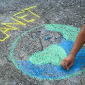 Person zeichnet den Planet Erde mit Kreide auf Asphalt