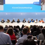 Bei den SB Klima-Zwischenverhandlungen sitzen Diskutierende auf einem Podium vor einer Menge an Zuhörer:innen. Im Hintergrund steht #JuneClimateMeetings