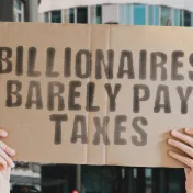 Zwei Hände halten ein Protestschild mit der Aufschrift "Billionaires barely pay taxes"