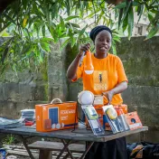 Eine Frau in einem Shirt der Solar Sisters hält eine Glühbirne hoch