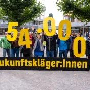 Zukunftskläger:innen halten gelbe Ziffern "5.400" in die Höhe
